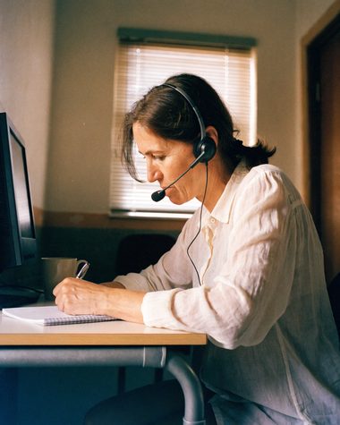 A Client Success Advocate at her desk, headset on, taking notes mid-call.