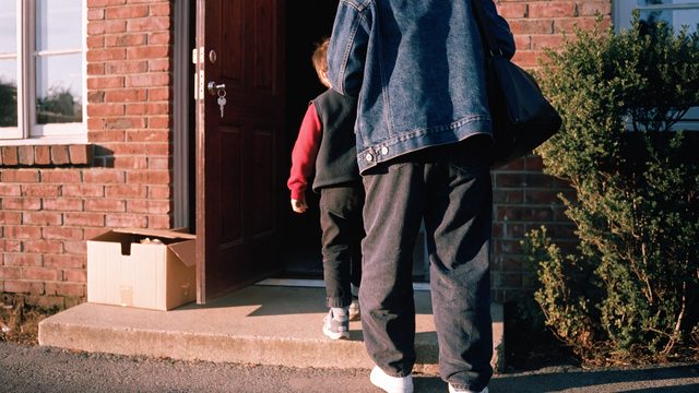 A parent and child stepping through their front door, keys still in the lock.