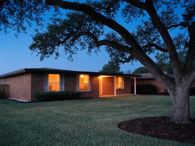 A brick home at dusk with the porch light on and warm light in the windows.